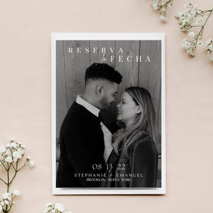 Può includere: Foto in bianco e nero di una coppia davanti a un muro di legno. Il testo "RESERVA LA FECHA" è in alto nell'immagine. La data "08 13 22" è sotto la coppia, insieme ai nomi "STEPHANIE + EMANUEL" e la posizione "BROOKLYN, NUEVA YORK".