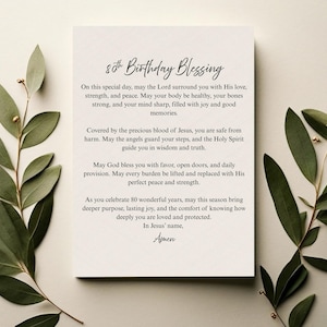 以下が含まれることがあります： エレガントな筆記体で「80th Birthday Blessing」と書かれたクリーム色のカード。カードは緑の葉の枝に囲まれています。テキストには誕生日のメッセージと祈りが含まれています。