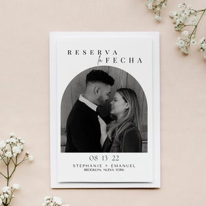 May include: A black and white photograph of a couple in a rounded archway. The text "RESERVA la FECHA" is at the top of the card. The date "08 13 22" is below the photo, followed by the names "STEPHANIE + EMANUEL" and the location "BROOKLYN, NUEVA YORK".