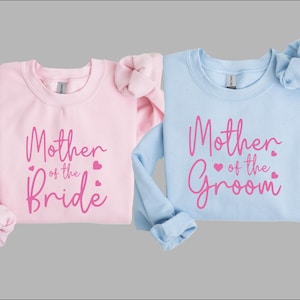 May include: Two sweatshirts, one pink and one light blue, with the text "Mother of the Bride" and "Mother of the Groom" in pink lettering.