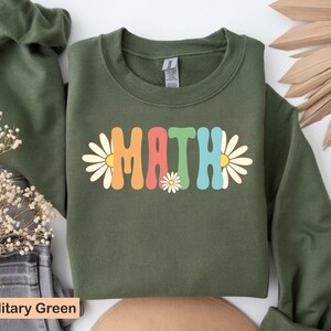 May include: A green sweatshirt with the word "MATH" in colorful retro letters and daisy flowers on the front. The sweatshirt is a crew neck style with long sleeves.