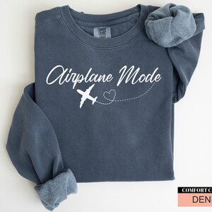 May include: A denim blue sweatshirt featuring the text "Airplane Mode" in white script, with a white airplane graphic and a dotted heart trail. The sweatshirt has long sleeves and a Comfort Colors tag.