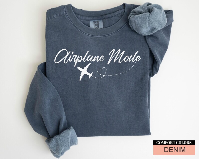 May include: A denim blue sweatshirt featuring the text "Airplane Mode" in white script, with a white airplane graphic and a dotted heart trail. The sweatshirt has long sleeves and a Comfort Colors tag.