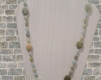 May include: A necklace made of light blue, green, and beige oval-shaped stones. The necklace is displayed on a white mannequin bust.