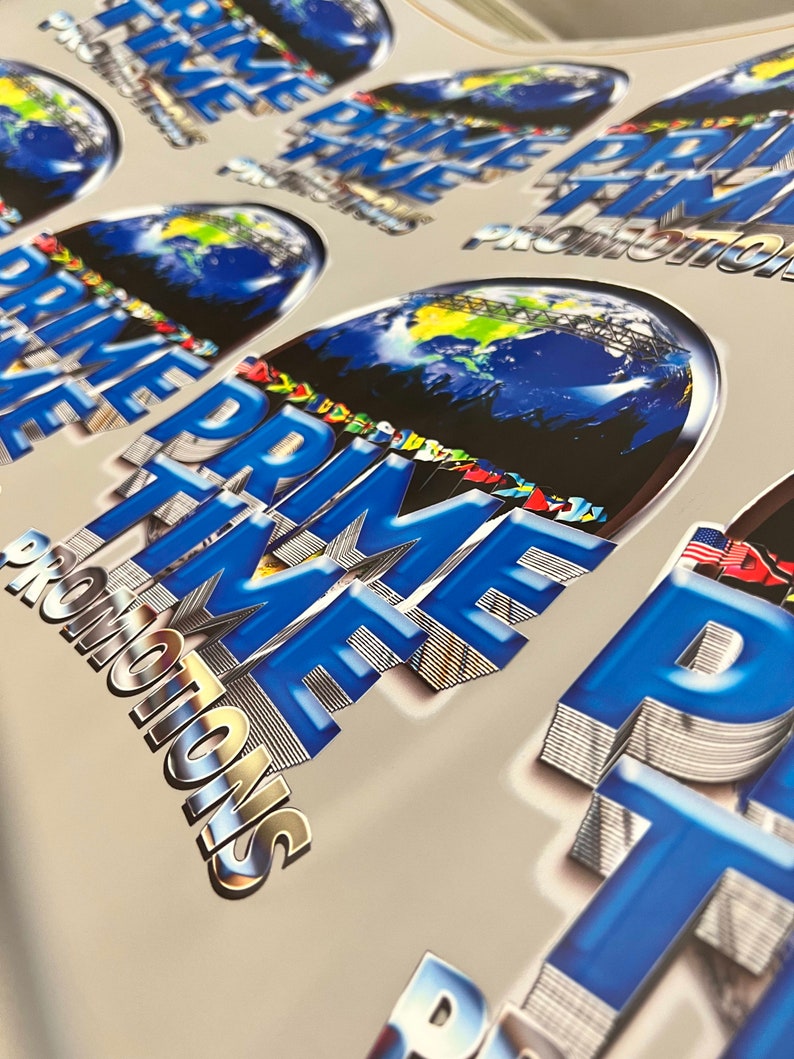 Pu&ograve; includere: Primo piano di un mucchio di adesivi blu e argento con il testo "PRIME TIME PROMOTIONS" e una grafica di un globo terrestre.