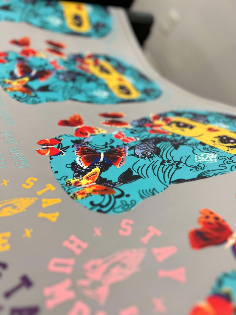 Pu&ograve; includere: Primo piano di un design stampato con un teschio turchese con farfalle colorate e motivi floreali. Il testo "Stay True" &egrave; visibile nell'angolo in basso a destra.