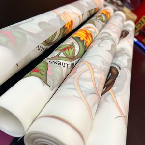 Pu&ograve; includere: Tre stampe botaniche arrotolate su sfondo bianco con fiori e foglie colorati. Le stampe hanno un bordo arcobaleno e il testo "WELLNESS" &egrave; visibile su una delle stampe.