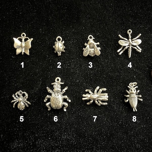 May include: A collection of silver-toned insect charms, including a butterfly, ladybug, bee, dragonfly, spider, beetle, spider, and cicada. A penny is included for size comparison. The charms are numbered 1 through 8.