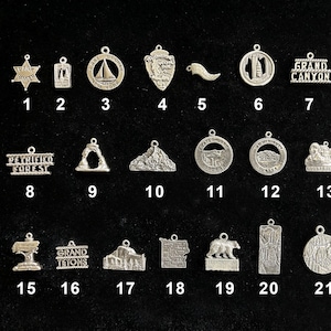 May include: A collection of 22 silver charms featuring various national park designs, including Grand Canyon, Bryce Canyon, Petrified Forest, and Grand Tetons. Each charm is numbered for easy identification.