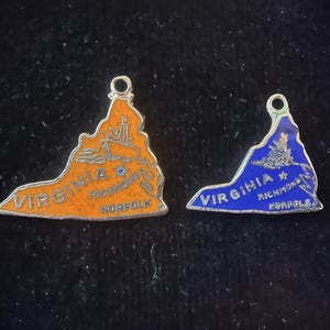 Puede incluir: Dos abalorios de plata con forma del estado de Virginia. Un abalorio es naranja con las palabras "VIRGINIA RICHMOND NORFOLK" y una estrella. El otro abalorio es azul con las palabras "VIRGINIA RICHMOND NORFOLK" y una estrella.