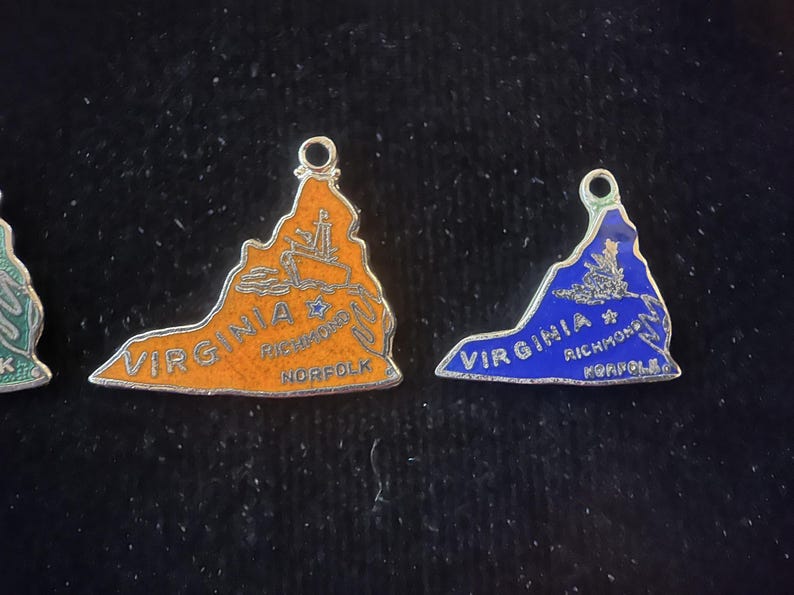Puede incluir: Dos abalorios de plata con forma del estado de Virginia. Un abalorio es naranja con las palabras "VIRGINIA RICHMOND NORFOLK" y una estrella. El otro abalorio es azul con las palabras "VIRGINIA RICHMOND NORFOLK" y una estrella.