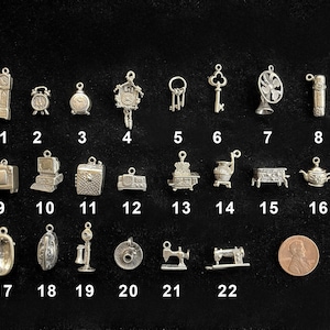 May include: A collection of small, silver-colored charms in various shapes, including clocks, keys, a fan, a TV, a computer, a sewing machine, and a teapot. A penny is included for size comparison.