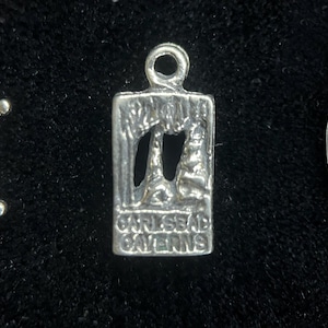 May include: Silver charm with a detailed image of Carlsbad Caverns, a national park in New Mexico. The charm is rectangular and has a loop at the top for attaching to a bracelet or necklace.