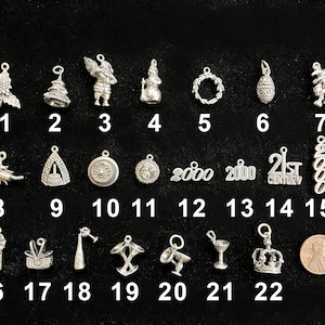 May include: A collection of small, silver-toned charms, each with a unique design. The charms include a holly sprig, Christmas tree, Santa Claus, snowman, wreath, pine cone, and more. A penny is included for size reference.