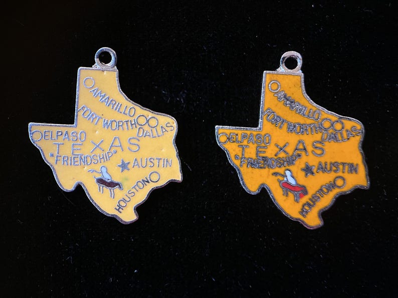Puede incluir: Dos colgantes de plata con forma del estado de Texas. Los colgantes son amarillos con letras negras y un dise&ntilde;o rojo y blanco. Los colgantes dicen "Texas" y "Friendship" en ellos. Los colgantes est&aacute;n sobre un fondo negro.
