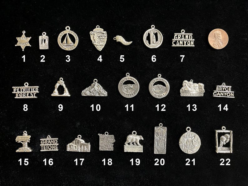 May include: A collection of 22 silver charms featuring various national park designs, including Grand Canyon, Bryce Canyon, Petrified Forest, and Grand Tetons. Each charm is numbered for easy identification.