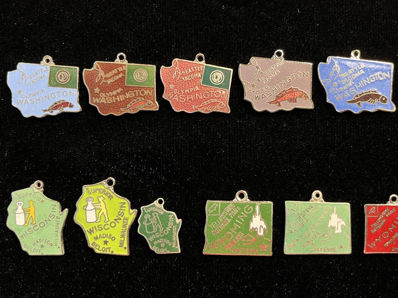 Puede incluir: Una colecci&oacute;n de 11 colgantes de estado de esmalte. Los colgantes tienen la forma de los estados de Washington, Wisconsin, Wyoming y Oreg&oacute;n. Los colgantes est&aacute;n decorados con esmalte de colores y presentan varios s&iacute;mbolos estatales, incluidos peces, una botella de leche y una cordillera.
