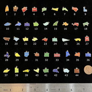May include: A set of 44 gold-colored metal charms shaped like different states in the United States. Each charm is painted with a different color and has the state name written on it. The charms are arranged in rows on a black surface.