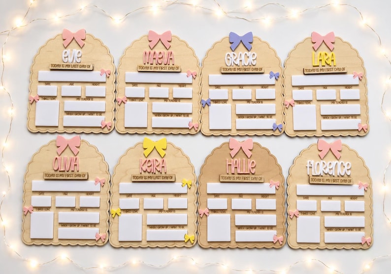May include: Eight arched wooden signs for school milestones, each featuring a name, a bow at the top, and smaller bows on the sides. The signs include white rectangular spaces for writing details like date, age, height, favorite things, teacher, and future career goals.