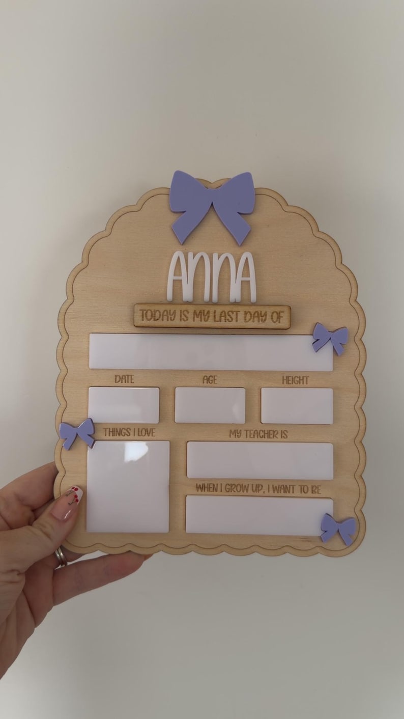 May include: A light-colored wooden arch-shaped sign featuring the name Anna in white lettering. The board includes the text Today is my last day of, Date, Age, Height, Things I love, My teacher is, and When I grow up, I want to be, with white panels.