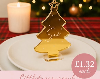 May include: A gold-colored acrylic Christmas tree ornament featuring a star at the top and small star accents. The name "Sue" is written in white cursive script across the center of the tree. The ornament is mounted on a clear rectangular base.