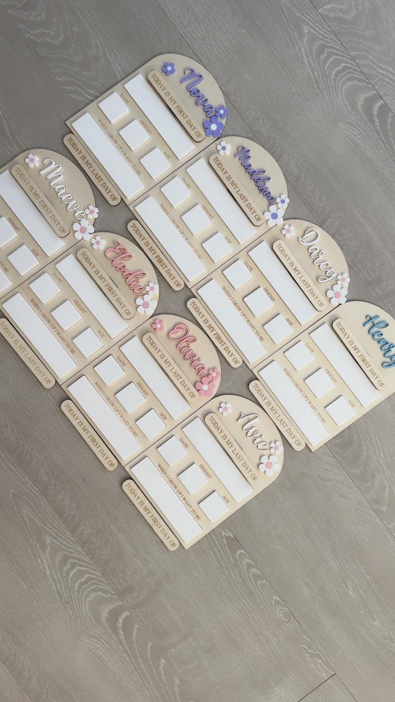 May include: Wooden milestone boards with names like Nova, Maeve, and Elodie, decorated with floral accents. Each board has spaces for date, height, and age, with the phrases "Today is my first day of" and "Today is my last day of".