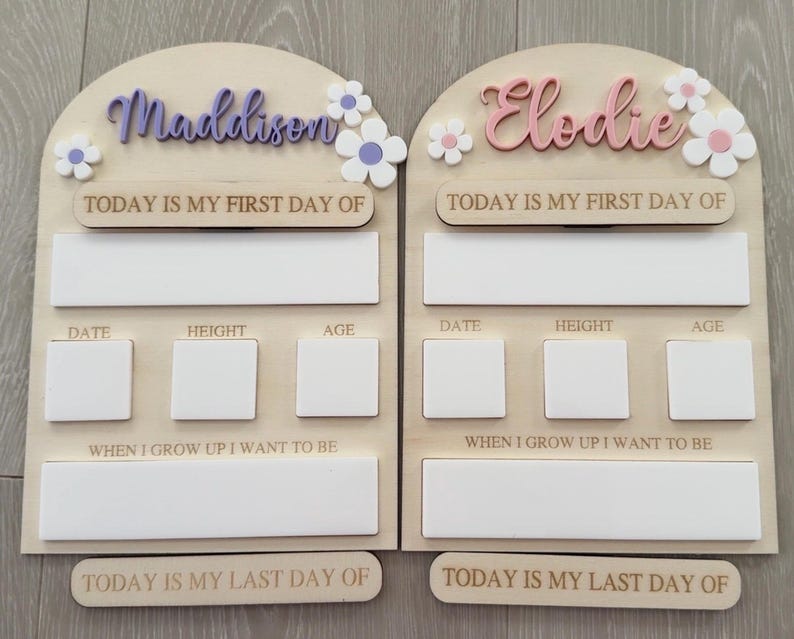 May include: Two wooden first and last day of school signs. One sign has the name "Maddison" in purple script with white and purple flowers. The other sign has the name "Elodie" in pink script with white and pink flowers. Each sign has space for date, height, age, and a statement.