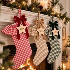 May include: Three Christmas stockings in red, tan, and dark green gingham patterns. Each stocking features a ruffled cuff, a velvet bow, and a wooden star-shaped tag engraved with the names Ella, Oliver, and Arthur, hanging from a fireplace.