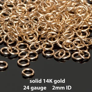 Könnte beinhalten: Ein Haufen kleiner, glänzender, goldfarbener Sprungringe. Der Text auf dem Bild lautet "solid 14K gold, 24 gauge, 2mm ID". Diese Ringe eignen sich für die Schmuckherstellung und das Basteln.
