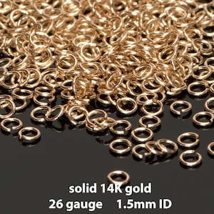 May include: A pile of small, shiny, gold-colored jump rings. The text on the image reads "solid 14K gold, 26 gauge, 1.5mm ID". These rings are used for jewelry making and other crafts.