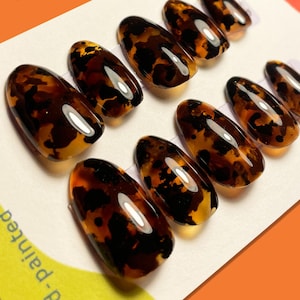 May include: Set of ten tortoise shell press-on nails. The nails are oval shaped and have a brown and black marbled pattern.