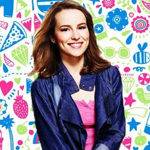 May include: A woman wearing a pink top, dark blue denim jacket, and distressed jeans. The background is a colorful pattern with the text "bridgit mendler".