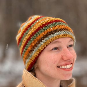 May include: A person wearing a colorful striped crocheted beanie hat. The hat has stripes of red, orange, yellow, green, brown, and gray.