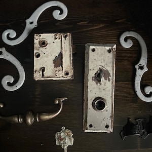 May include: Assortment of antique door hardware, including a white door knob, a white door latch, a brass door handle, and several white metal decorative pieces.
