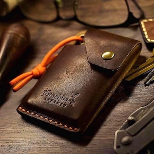 May include: A brown leather key holder with an orange cord and the text "Handmade" embossed on the front.