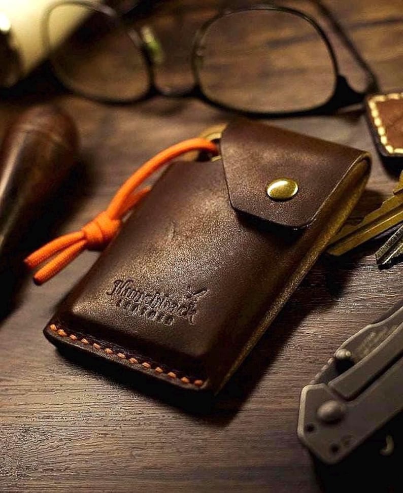 May include: A brown leather key holder with an orange cord and the text "Handmade" embossed on the front.