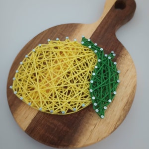 May include: A wooden cutting board with a yellow lemon and green leaves created using string art.