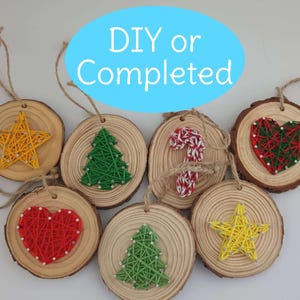 May include: A collection of wooden Christmas tree decorations with string art designs. The ornaments include a star, Christmas tree, candy cane, and heart. Each has a twine loop. The text "DIY or Completed" is in a blue oval.