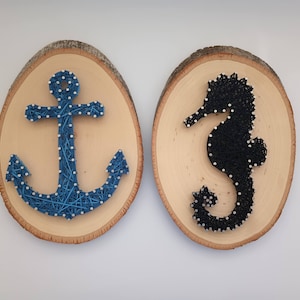 Könnte beinhalten: Zwei Holzrundlinge mit String-Art-Designs. Ein Rundling zeigt einen blauen Anker und der andere ein schwarzes Seepferdchen.