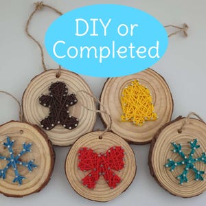 May include: A collection of wooden Christmas tree decorations with string art designs. The ornaments feature a gingerbread man, a bell, a bow, and snowflakes. Each is a wood slice with a twine hanger. The text "DIY or Completed" is in a blue oval.