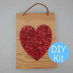 Peut inclure: Kit de bricolage pour art de la ficelle avec un motif de cœur rouge sur une planche de bois avec une poignée en corde de jute. Le kit comprend tous les matériaux nécessaires pour créer le motif du cœur, y compris des clous, de la ficelle et une planche de bois.