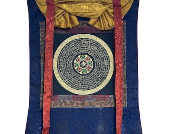 Puede incluir: Una rueda de oración tibetana tradicional con letras doradas y un diseño de mandala colorido. La rueda de oración está montada en un rodillo de madera y tiene un respaldo de seda azul con ribetes dorados y rojos.