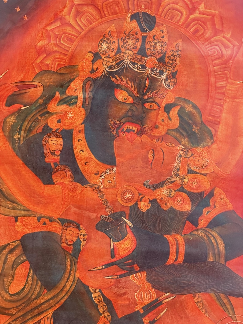 May include: A vibrant red and dark blue thangka painting depicting a wrathful deity in a fierce embrace with a consort. The figures are adorned with intricate jewelry, crowns, and skulls, set against a fiery red background with detailed line work.