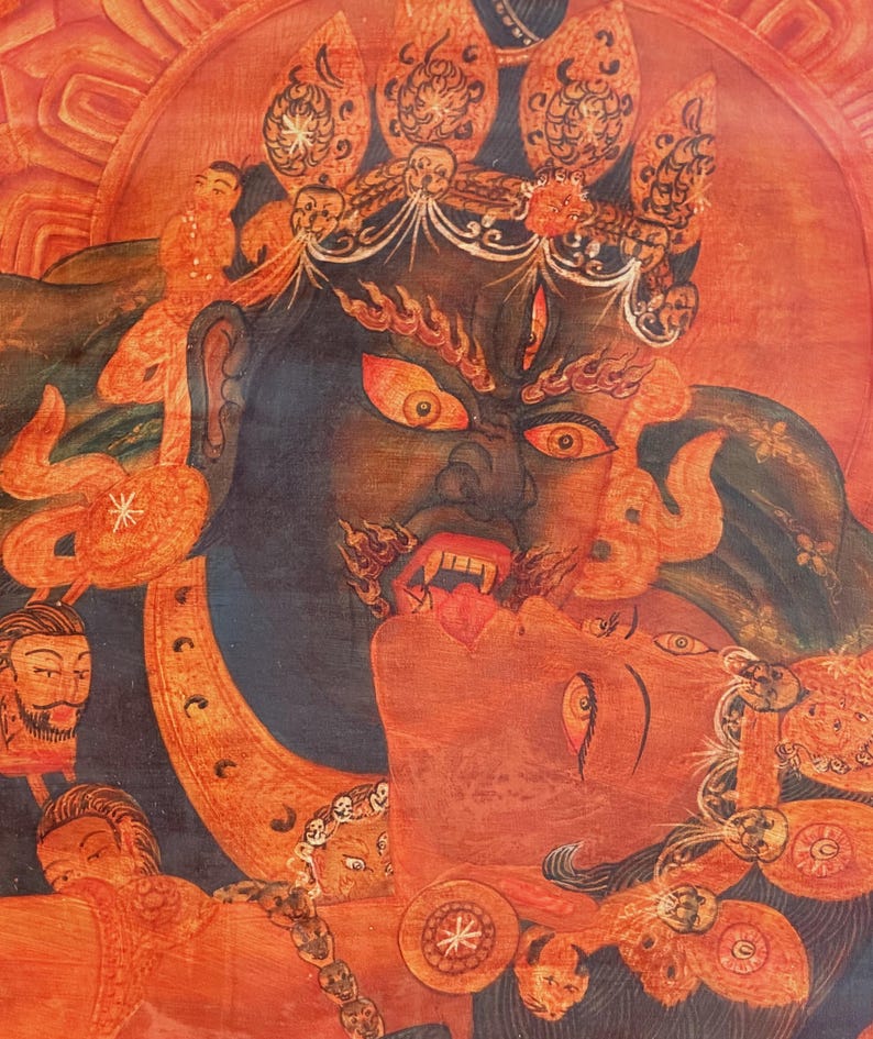 May include: A detailed thangka painting featuring a dark blue deity with a fierce expression, wide orange eyes, and bared teeth, embracing a red-skinned figure. The composition includes ornate golden crowns, skull motifs, and smaller faces.