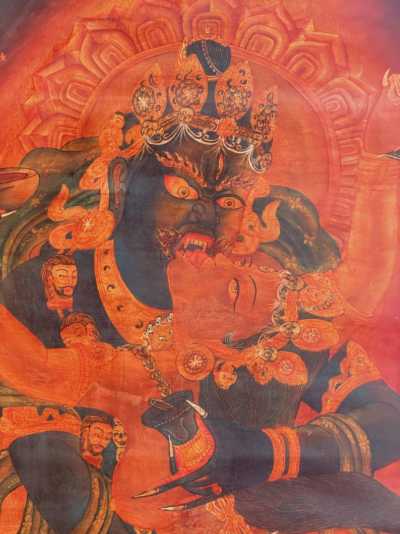 May include: A vibrant thangka painting featuring a dark blue deity with a fierce expression and bared teeth, embracing a red figure. The composition includes intricate golden crowns, jewelry, and a circular halo against a deep red background.