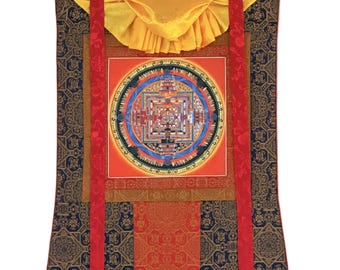 May include: A vertical wall hanging featuring a central circular mandala painting in shades of red, blue, and gold. The artwork is framed by layered fabric borders in navy blue, orange, and yellow, with two long red ribbons and a yellow top cover.