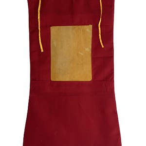 Pu&ograve; includere: Un arazzo da parete in tessuto rosso con un'apertura rettangolare che contiene un inserto in tessuto beige. L'arazzo ha due lacci in tessuto giallo nella parte superiore.