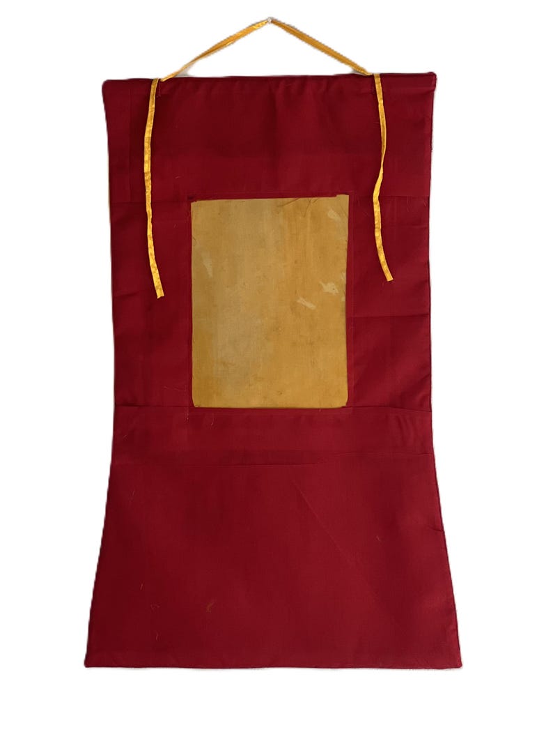 Pu&ograve; includere: Un arazzo da parete in tessuto rosso con un'apertura rettangolare che contiene un inserto in tessuto beige. L'arazzo ha due lacci in tessuto giallo nella parte superiore.