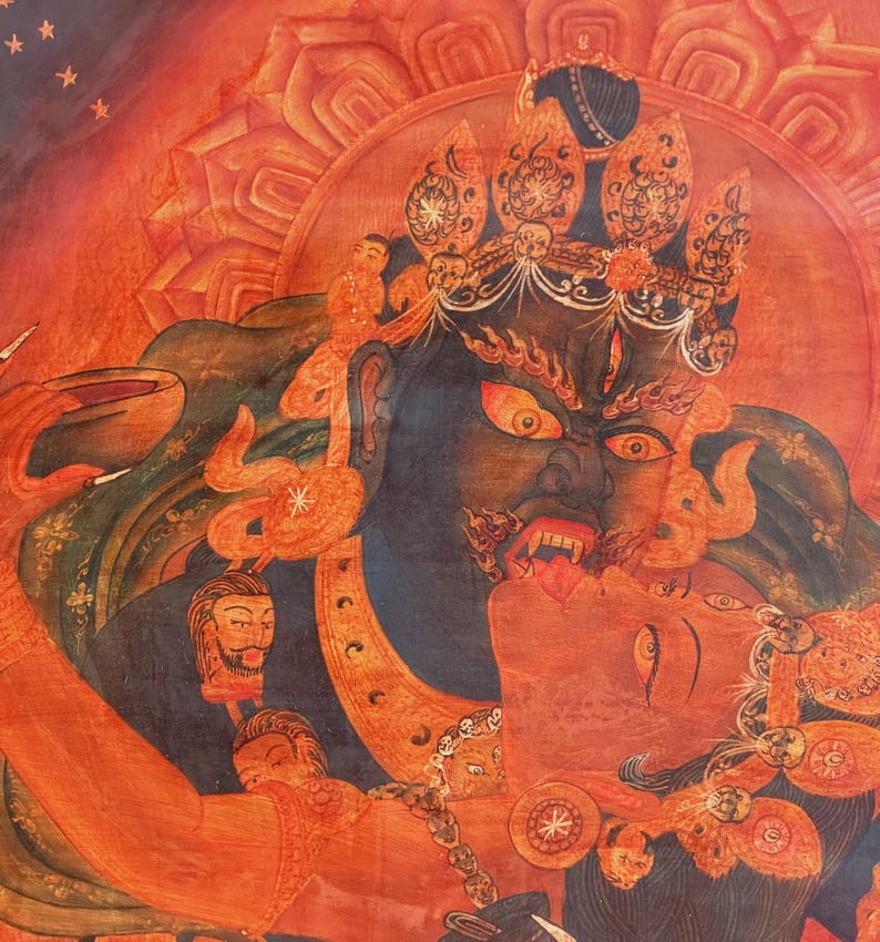 May include: A detailed thangka painting featuring a dark blue deity with a fierce expression, bared teeth, and a third eye, embracing a red figure. The artwork is rendered in vibrant shades of orange and red, adorned with intricate golden crowns.