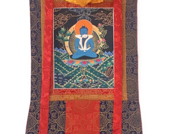 May include: A vertical fabric wall hanging featuring a central rectangular painting of a blue Buddha figure seated in a meditative pose on a lotus flower. The artwork is framed by layered borders of patterned blue, red, and gold silk fabric.